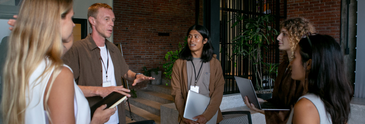 Five people in a circle with laptops discussing in a open space