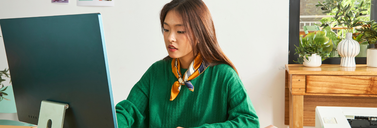 GST Calculator Header woman in green jumper at desk looking at computer