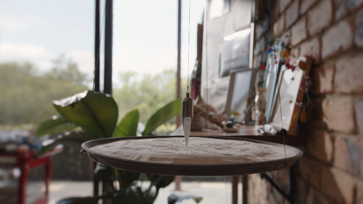 A crystal pendulum carving the sand
